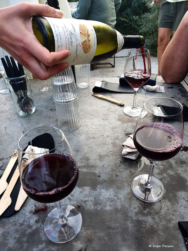 En hand håller i en flaska rött vin samtidigt som den fyller på ett glas. Två glas har redan rött vin i sig.