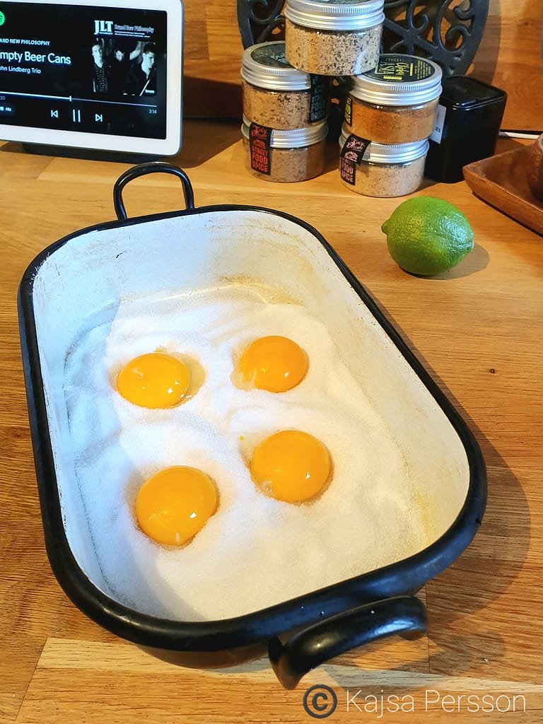 Fyra Äggulor på salt och sockerbädd i en svart ugnsform, ska bli garvade äggulor